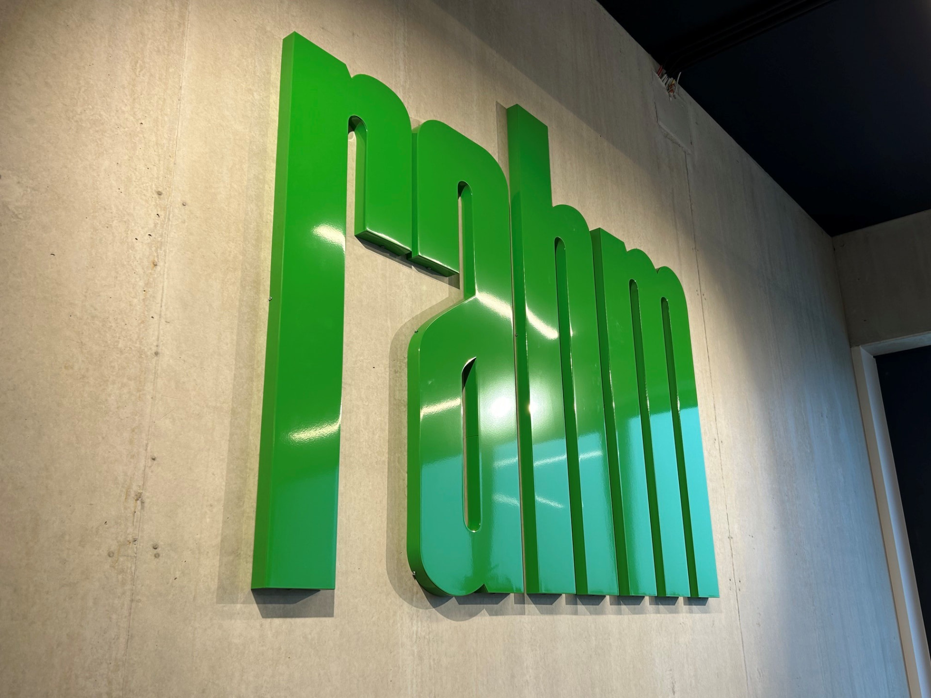 Grüne 3D-Buchstaben „rahm“ an einer Betonwand